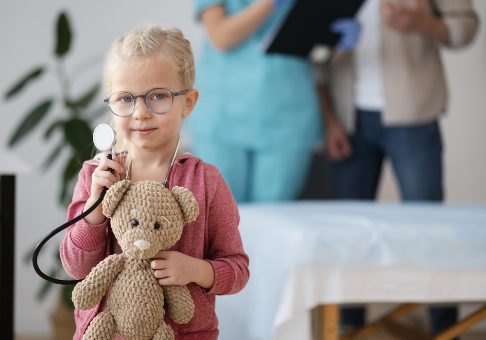 Una bambina nello studio pediatrico di Monteverde con uno stetoscopio al collo e un orsacchiotto di peluche in braccio